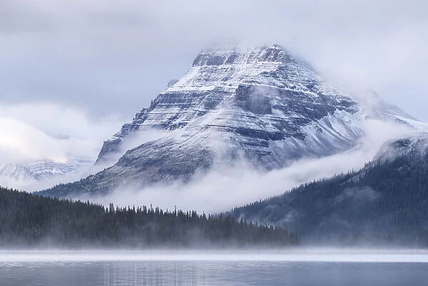 Snow dusted Bow Peak mountain surrounded by mist, viewed from across Bow Lake, Icefields