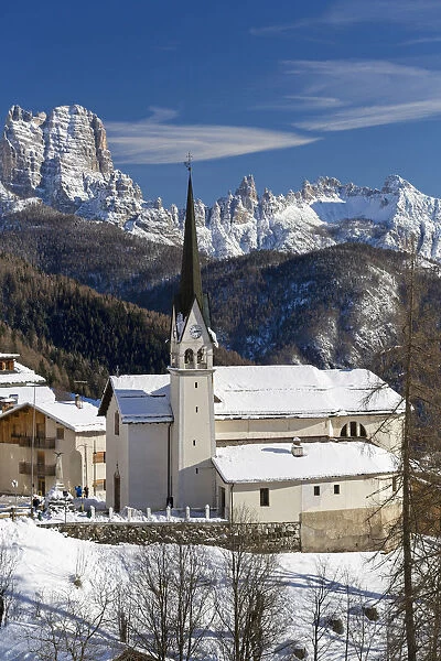 The snowy alpine village and church of Zoppa di Cadore framed by the peak of Bosconero
