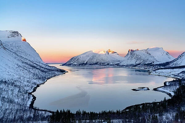 Snowy mountain peaks reflected in the frozen sea at dawn from Bergsfjord viewpoint, Senja, Troms county, Norway