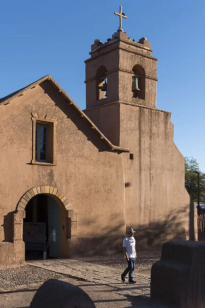 South America, Andes, Atacama, San Pedro de Atacama, Man walks past an Adobe church