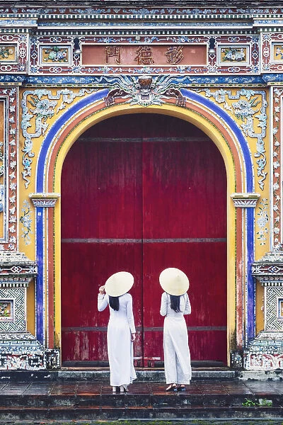 Southeast Asia, Vietnam, Hue. Two young women wearing Ao Dai dresses stand next to an