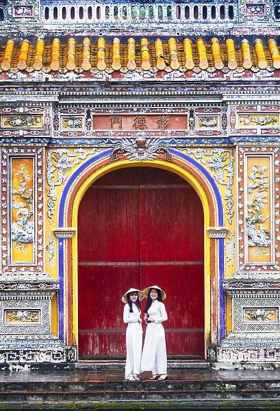 Southeast Asia, Vietnam, Hue. Two young women wearing Ao Dai dresses stand next to an