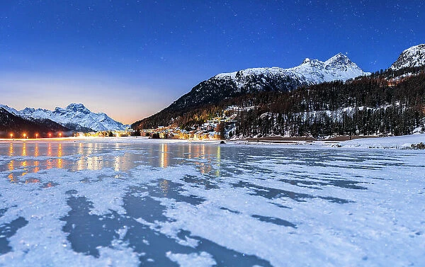 Starry sky over the snowy mountains and Silvaplana village seen from the frozen lake Champfer, Graubunden, Engadin, Switzerland