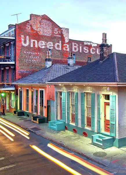 Streaking car lights at dusk on Dumaine Street in the French Quarter of New Orleans. The street and neighborhood contain many examples of the unique architecture found here as seen in the wood shutters and the Uneeda Biscuit sign. Louisiana, USA