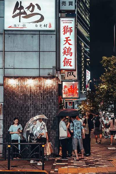 Summer night in Tokyo, Japan. People wait in line to enter the restaurant under the rain and illuminated signs