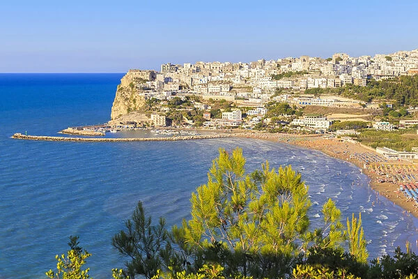The sun illuminates the ancient town of Peschici and its beach full of tourists. Apulia