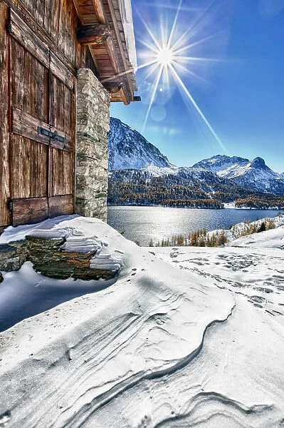 The sun is reflected in the Lake of Sils after an autumn snowfall from one of the
