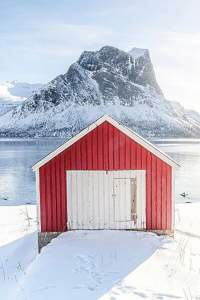 Sunlight over snowy mountains and fisherman cabin overlooking the arctic sea, Bergsfjord, Senja, Troms county, Norway