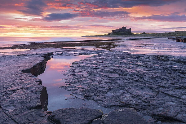 Sunrise over Bamburgh Castle from the rocky shores of Bamburgh Beach, Northumberland