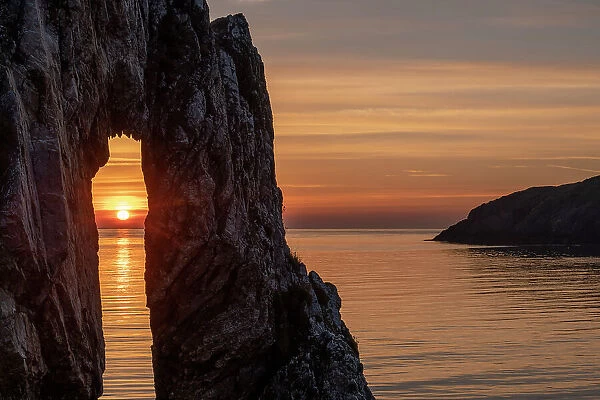Sunrise through a rock arch at the Victorian brickworks site at Porth Wen, Anglesey, Wales, UK. Spring (May) 2019