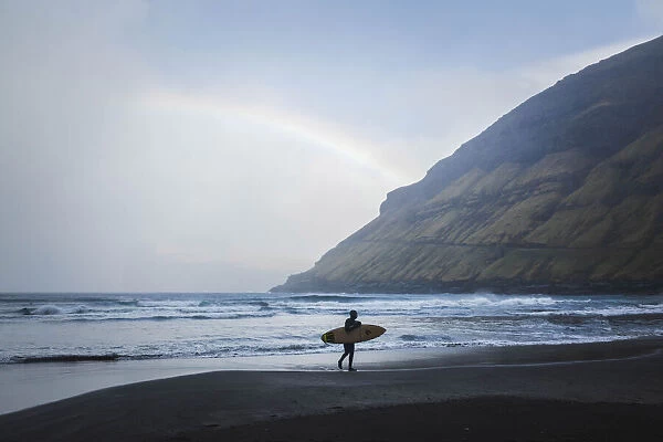 A surfer walking along the beach in Tjornuvik. Streymoy, Faroe Islands