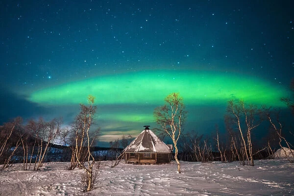 Swedish Lapland, Abisko National Park. Northern Lights over a typical teepee in the forest and snow, winter. Arctic Circle