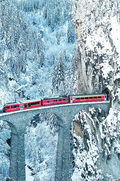 Swiss red train running on Landwasser viaduct from a tunnel carved on steep mountain, Filisur, Graubunden canton, Switzerland