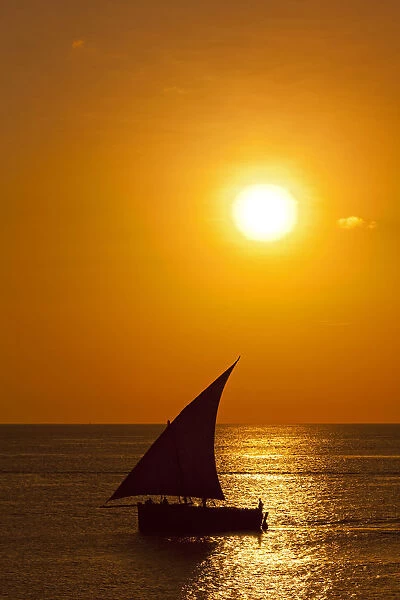 Tanzania, Zanzibar, Unguja, Stone Town. A Dhow sails out of the harbour at sunset