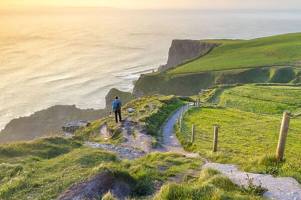 A tourist admiring the view of a sunset at the Cliffs of Moher