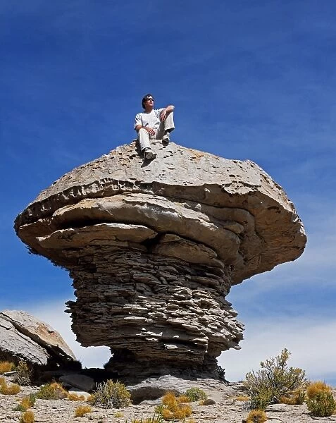 A tourist sits on top of a massive wind-eroded boulder