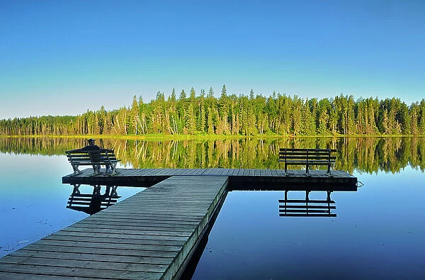 tourist sitting on bench admiring the view of a northern lake, Duck Mountain Provincial Park, Manitoba, Canada