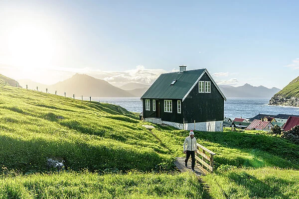 Tourist walking in the green landscape surrounding the coastal village of Gjogv, Eysturoy Island, Faroe Islands (MR)