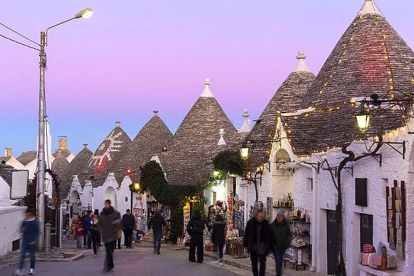 Tourist walks in the pedestrian area between trulli houses at twilight