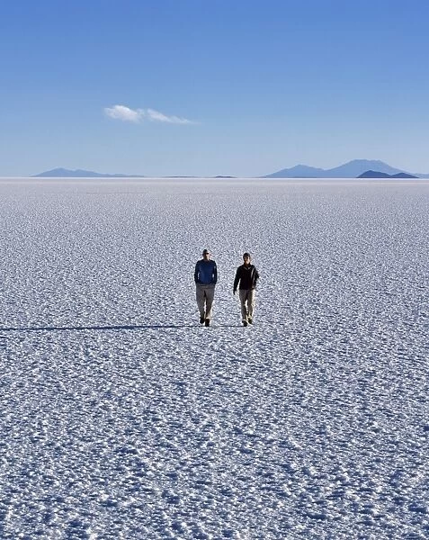 Two tourists walk across the endless salt crust of the Salar de Uyuni
