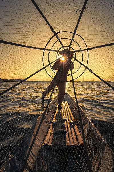Traditional leg-rowing fisherman viewed through conical fishing net rowing a boat on Lake