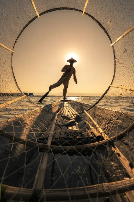 Framed Print : Traditional leg-rowing fisherman viewed through conical fishing net rowing a boat on Lake Framed Print : Traditional leg-rowing fisherman viewed through conical fishing net rowing a boat on Lake
