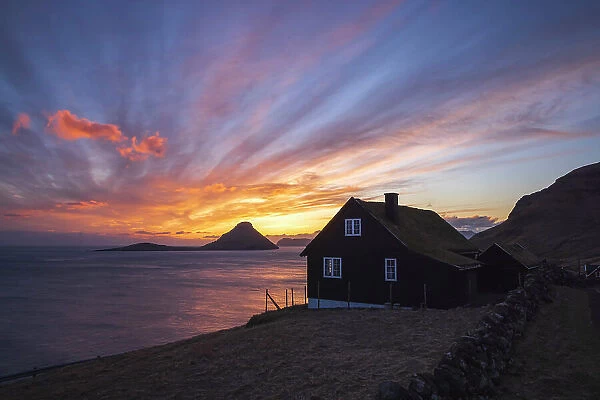 A traditional turf house and a spectacular sunset in Velbastaður. Island of Streymoy. The island of Koltur in the background. Faroe Islands