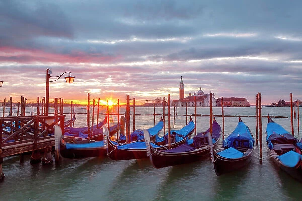 Some traditional venetian gondolas moored at Riva degli Schiavoni at dawn with St. george Island on the backgrund, Venice, Veneto, Italy
