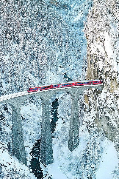 Train on Landwasser viaduct entering in a tunnel carved into a snowy mountain ridge, Filisur, Graubunden canton, Switzerland