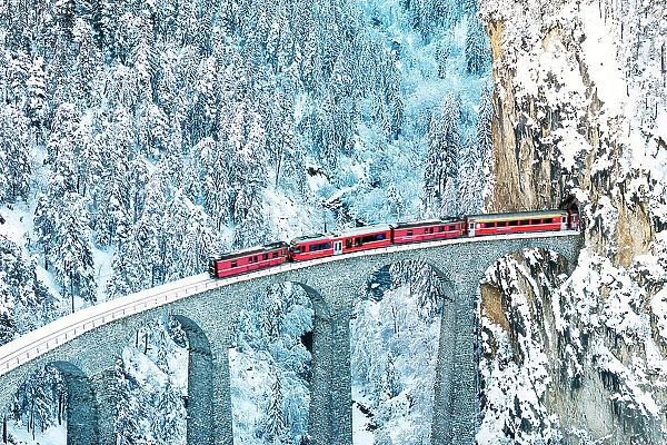 Train on Landwasser viaduct entering in a tunnel carved into a mountain ridge in winter, Filisur, Graubunden canton, Switzerland