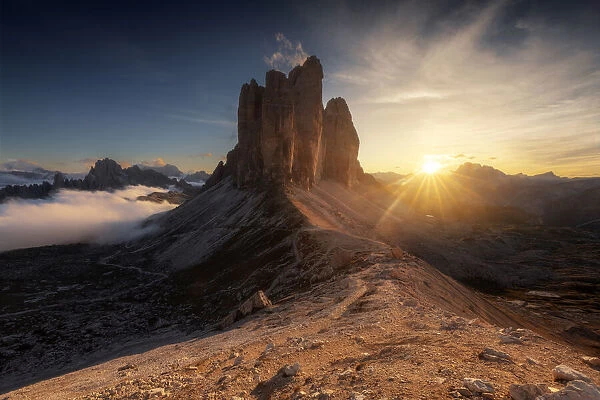 The Tre Cime di Lavaredo lined up from the Forcella Lavaredo during a cold late summer sunset, with the Cadini di Misurina emerging from the fog on the left. Dolomites, Italy