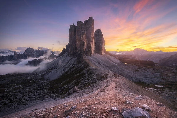 The Tre Cime di Lavaredo lined up from the Forcella Lavaredo during a cold late summer sunset, with the Cadini di Misurina emerging from the fog on the left. Dolomites, Italy