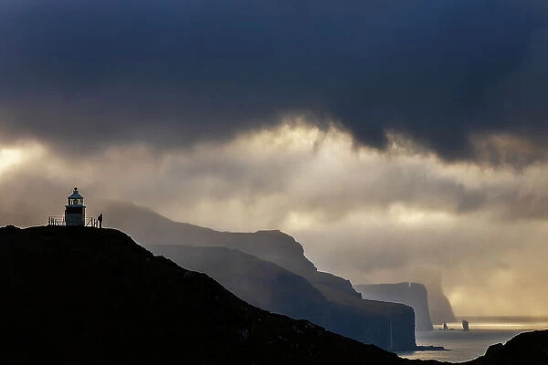 A trekker at Kallur lighthouse with a scenic view at sunset, Kalsoy, Faroe Islands, Denmark