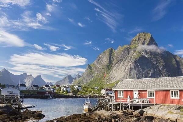 Typical house of fishermen called Rorbu framed by rocky peaks and blue sea Reine