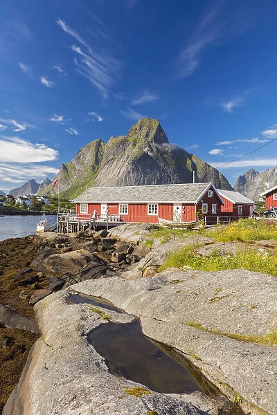 Typical houses of fishermen called Rorbu framed by rocky peaks and blue sea Reine