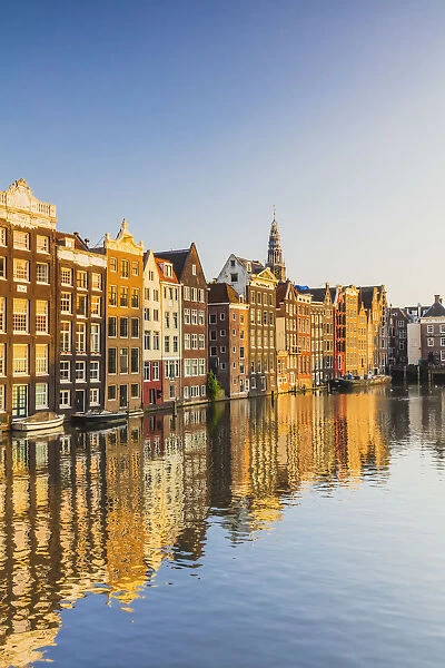 Typical houses reflecting in Damrak water canal at sunset in Amsterdam