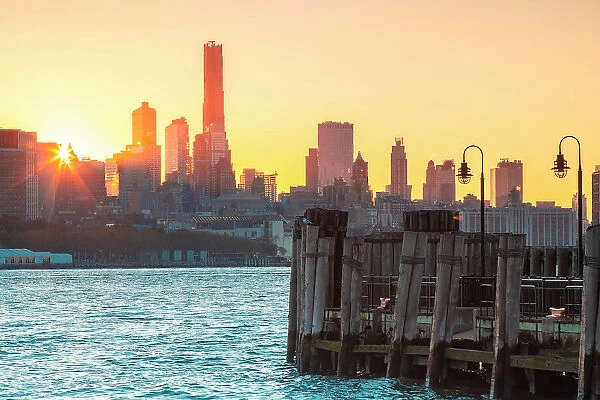 USA, New York City, view of the sun rising behind the buildings of Lower Manhattan with an old pier in Jersey city in the foreground