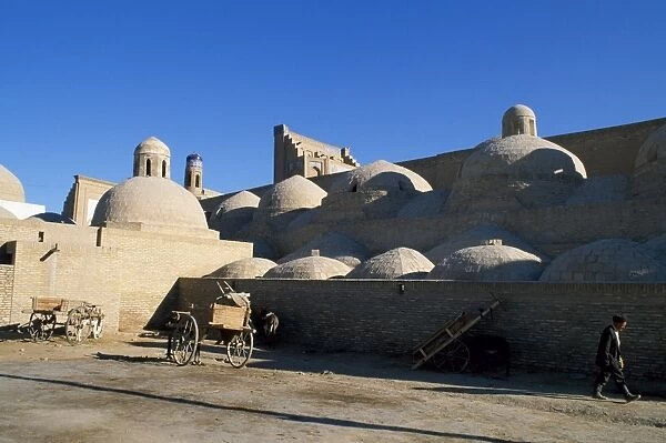An Uzbek man walks beside the many domed walls of the Ichan Kala