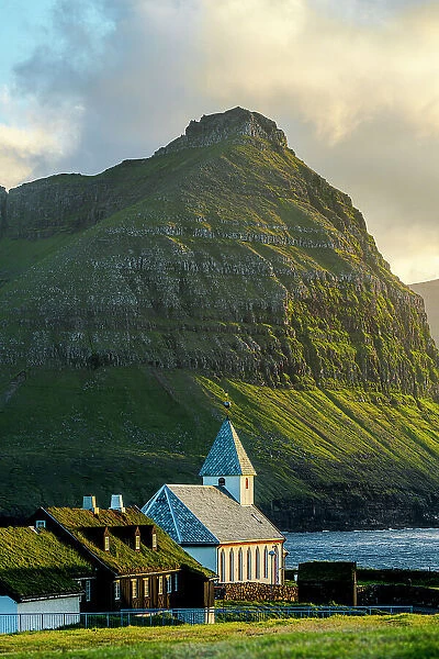 Vidareidi church and grass roof houses framed by majestic mountains of Bordoy island, Vidoy Island, Faroe Islands