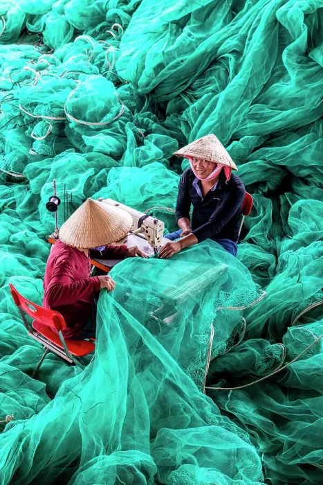Framed Print : Vietnam, Cam Ranh, two men repair green fishing nets using a sewing machine Framed Print : Vietnam, Cam Ranh, two men repair green fishing nets using a sewing machine
