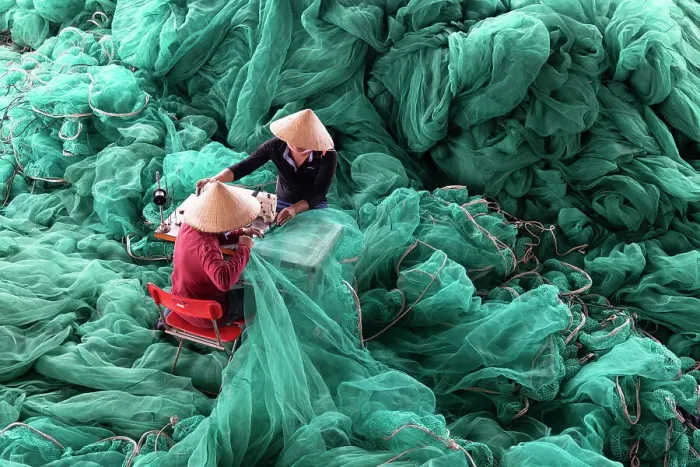 Framed Print : Vietnam, Cam Ranh, two men repair green fishing nets using a sewing machine
