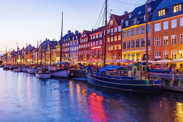 View of colored houses reflecting in Nyhavn water canal by night in Copenhagen, Denmark