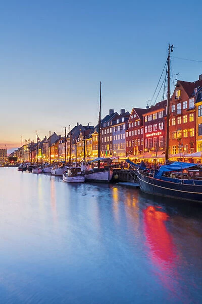 View of colored houses reflecting in Nyhavn water canal by night in Copenhagen, Denmark
