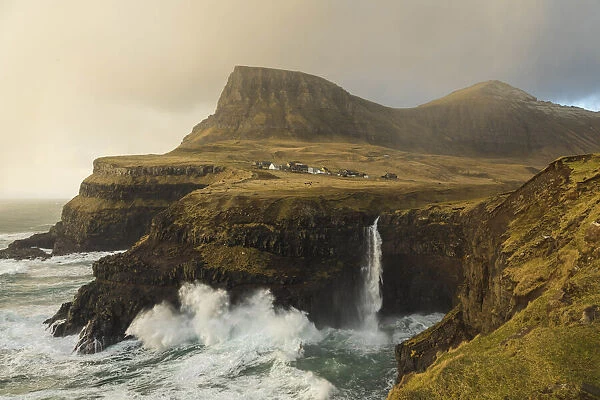 The village of Gasadalur and its waterfall, at sunset, while they are hit by strong winds. Vagar, Faroe Islands