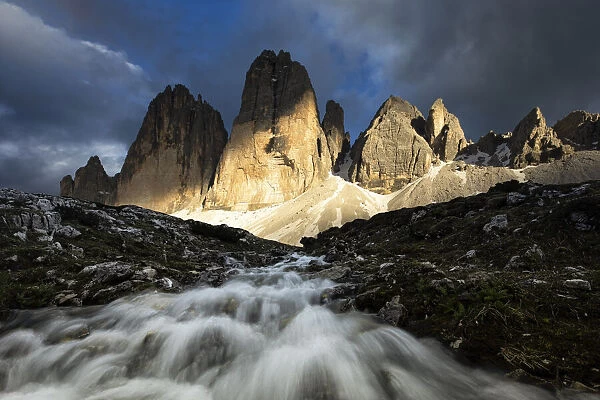 a warm light filters through the clouds and envelops the Tre Cime di Lavaredo during a