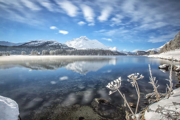 Winter clouds dancing in the wind reflecting in Lake Sils. Engadine. Switzerland