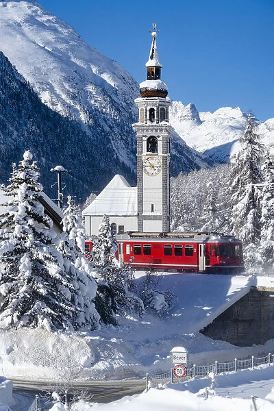Winter sun over Bernina Express train and church bell tower of Bever village covered with
