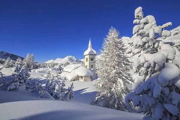 The winter sun illuminate the snowy landscape and the typical church Maloja Canton
