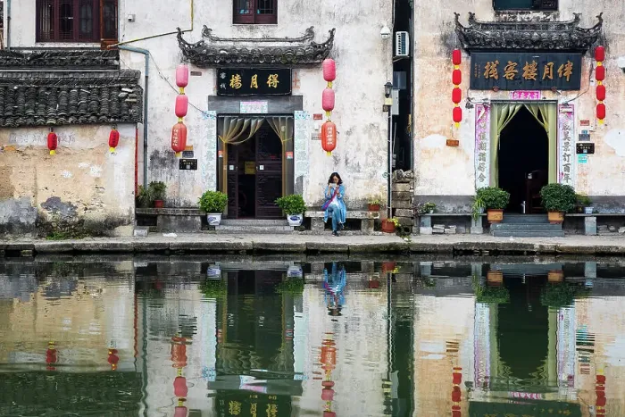 Framed Print : Woman on bench and village buildings reflected in pond, Hongcun, China