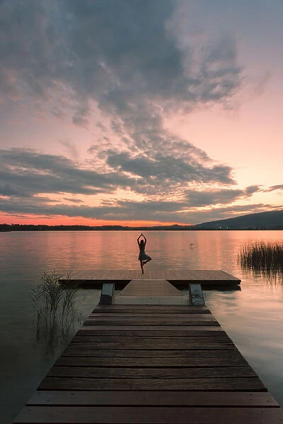 Woman dancing on a Wood pier on Pusiano lake at sunset, Bosisio Parini, Lecco province